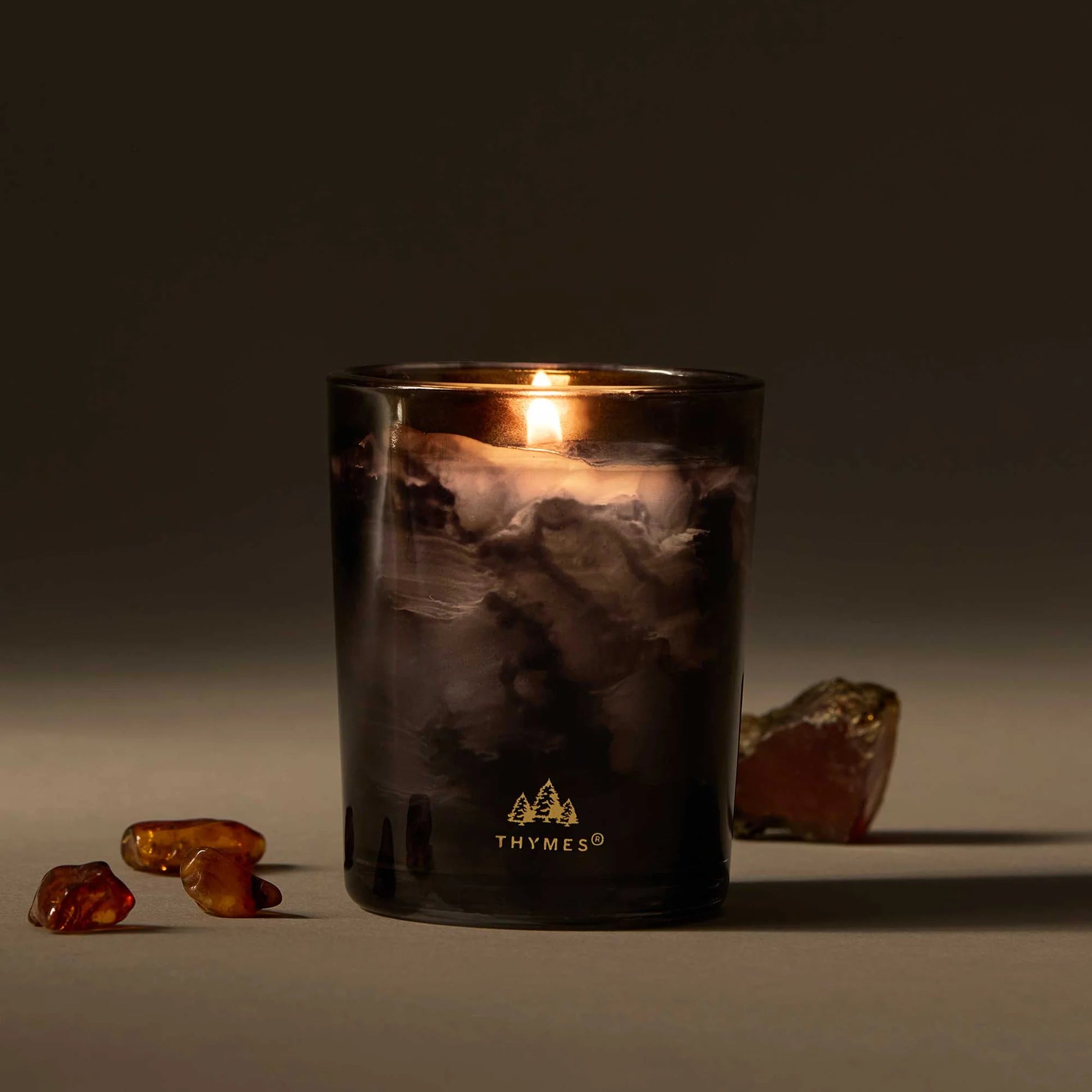 A Lit Noir Woods Votive Candle On Table