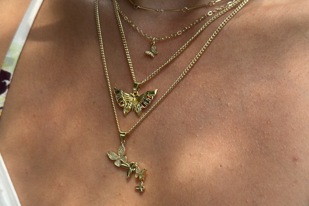 Close-up of a person wearing multiple gold necklaces with butterfly pendants on a light skin background.
